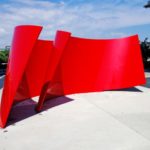 A Bright Shiny Red Metal Sculpture Resembling Two Pieces Of Ribbon In A Semi-Circle Showing The Path Between Them