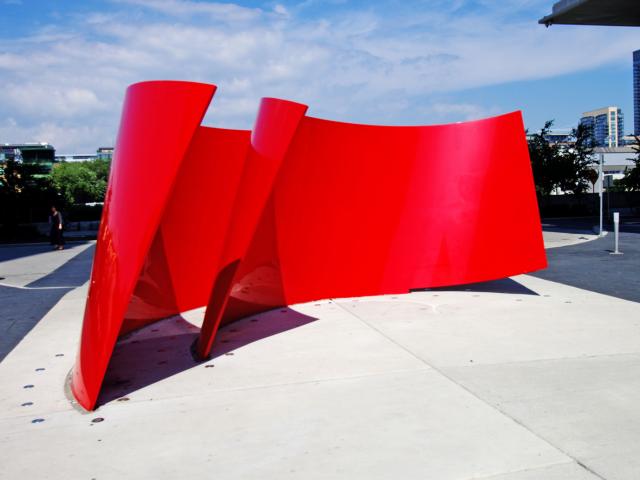 A Bright Shiny Red Metal Sculpture Resembling Two Pieces Of Ribbon In A Semi-Circle Showing The Path Between Them