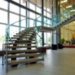 A Set Of Custom Fabricated Curved Architectural Stairs With Glass Side Panels And Stainless Steel Railings In A Building Lobby