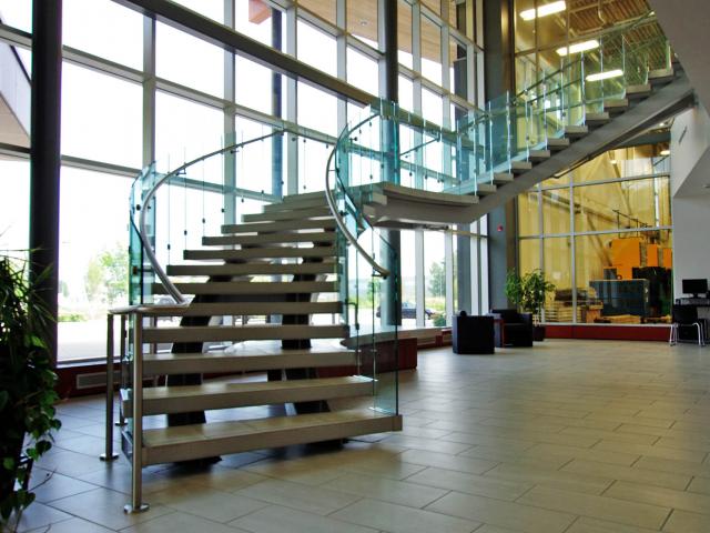 A Set Of Custom Fabricated Curved Architectural Stairs With Glass Side Panels And Stainless Steel Railings In A Building Lobby