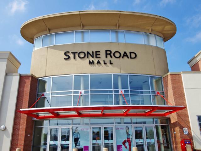 A Red Metal Awning With Rectangular Glass Panels Attached Over The Entrance To The "Stone Road Mall"