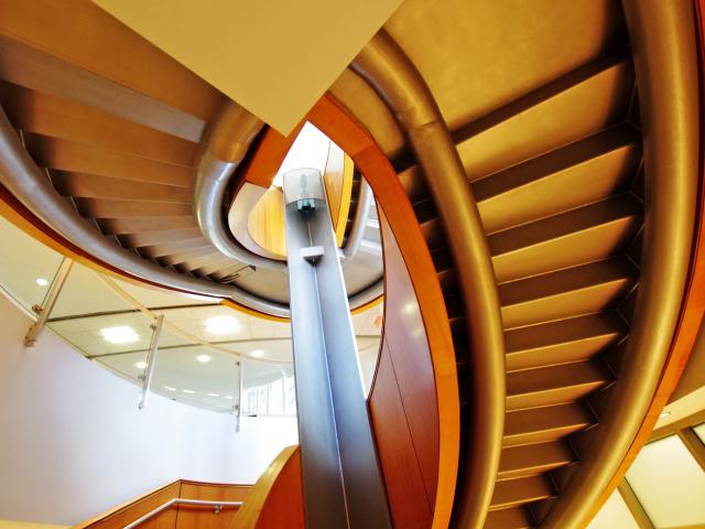 Looking Up At The Underside Of An Oval Shaped Multi Floor Switchback Staircase With A Pair Of Curved Pipe Sections Supporting It