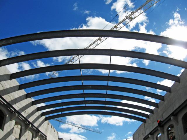 Looking Up At Rolled Steel Structural Roof Sections In Front Of A Cloudy Blue Sky