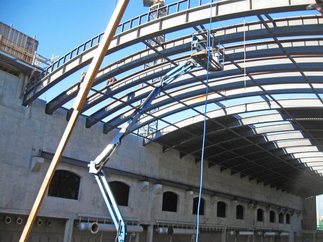 Looking Up At Rolled Structural Steel Roof Sections Being Installed At A Construction Site