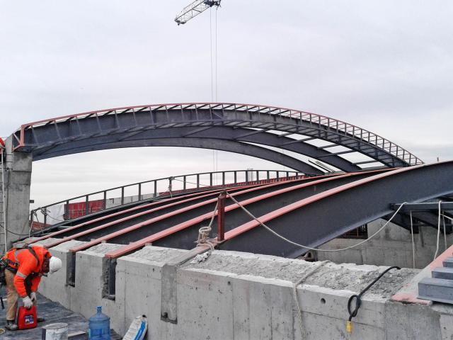 A Worker Installs Rolled Structural Steel Roof Sections At A Building Construction Site