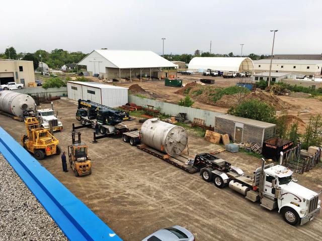 An Aerial View Of Two Cylindrical Vessels For Bisulfate Storage With Flange Attachments Are Loaded Onto Trucks In A Yard