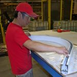 Un travailleur vérifie un canal en aluminium plié personnalisé par rapport à un modèle dans un atelier d'acier Kubes