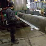 Un trabajador verifica una sección de tubería de gran diámetro contra una plantilla en la máquina dobladora por inducción en Kubes Steel