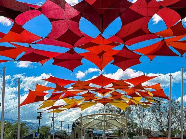 A Sun Shade In An Outdoor Park Supported By Upright Columns And A Circular Overhead Frame