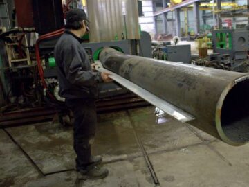 Un travailleur vérifie une section de tuyau de grand diamètre par rapport à un modèle dans la machine à cintrer par induction à Kubes Steel